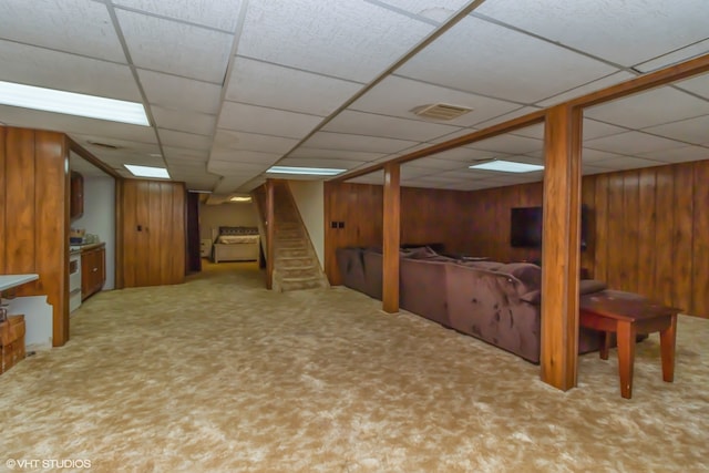 basement with a paneled ceiling, wooden walls, and carpet