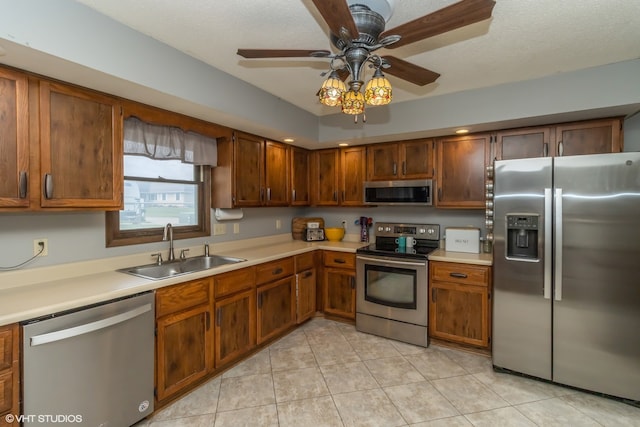 kitchen featuring a textured ceiling, light tile patterned floors, stainless steel appliances, sink, and ceiling fan