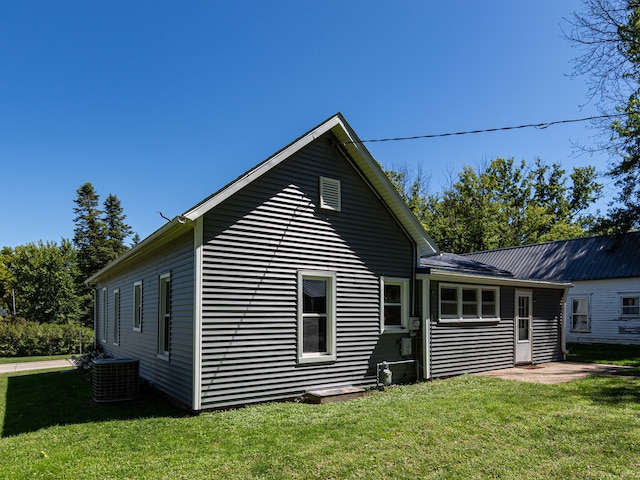 rear view of house with central air condition unit and a lawn