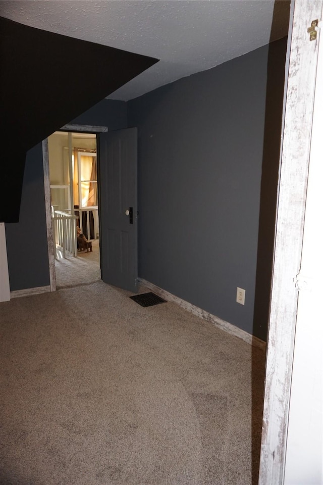 carpeted spare room featuring visible vents, a textured ceiling, and baseboards