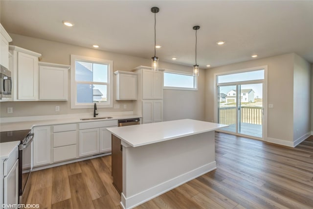 kitchen featuring a kitchen island, white cabinetry, stainless steel appliances, sink, and light wood-type flooring