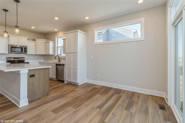 kitchen with stainless steel appliances, decorative light fixtures, light wood-type flooring, white cabinets, and a center island