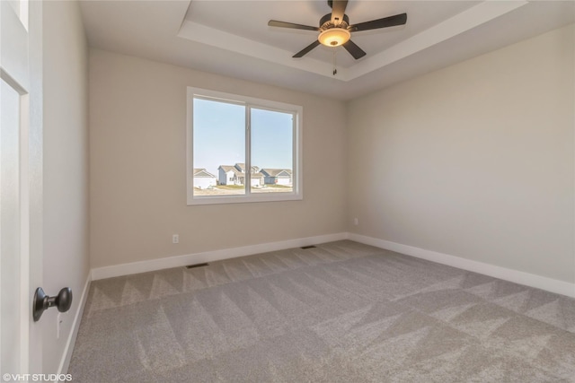 unfurnished room featuring ceiling fan, light colored carpet, and a tray ceiling