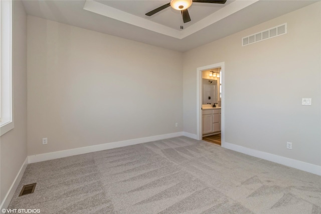 empty room featuring light carpet, ceiling fan, and a raised ceiling