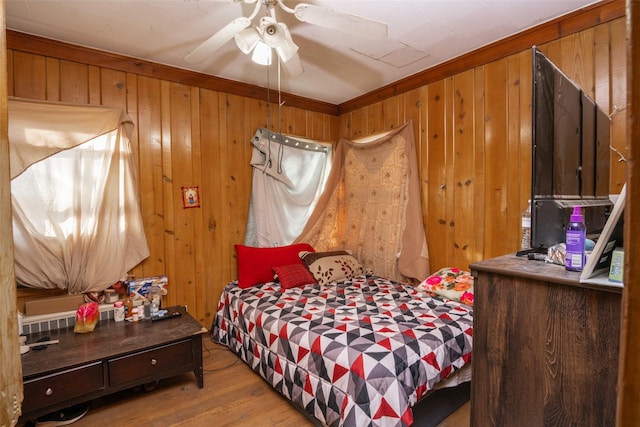 bedroom featuring wooden walls, hardwood / wood-style flooring, ceiling fan, and crown molding