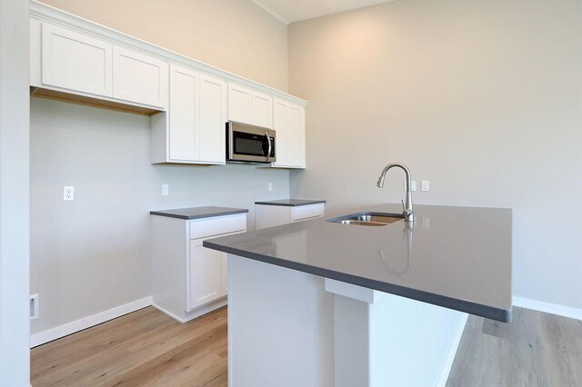 kitchen featuring light wood-type flooring, an island with sink, white cabinetry, and sink