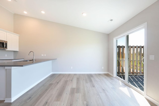 kitchen featuring stainless steel microwave, visible vents, white cabinets, a sink, and baseboards