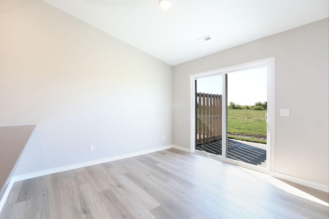 unfurnished room featuring vaulted ceiling, light wood finished floors, visible vents, and baseboards