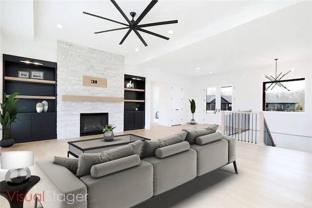 living room with a fireplace, light hardwood / wood-style floors, a chandelier, and built in shelves