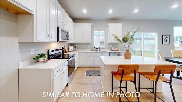 kitchen with a kitchen bar, appliances with stainless steel finishes, light wood-type flooring, a center island, and white cabinetry