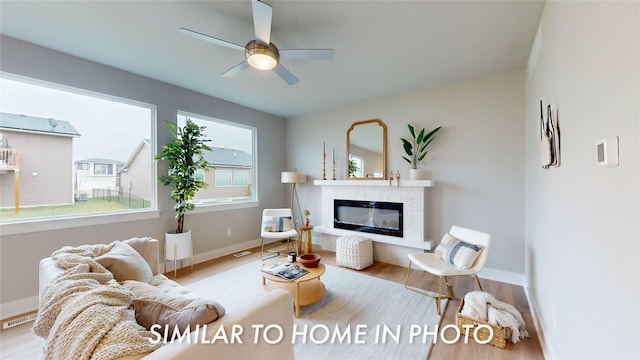 living room featuring ceiling fan, a fireplace, and light wood-type flooring