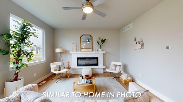 living room featuring a high end fireplace, light hardwood / wood-style floors, and ceiling fan