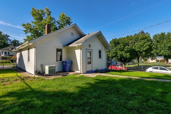 rear view of property featuring a lawn and central air condition unit