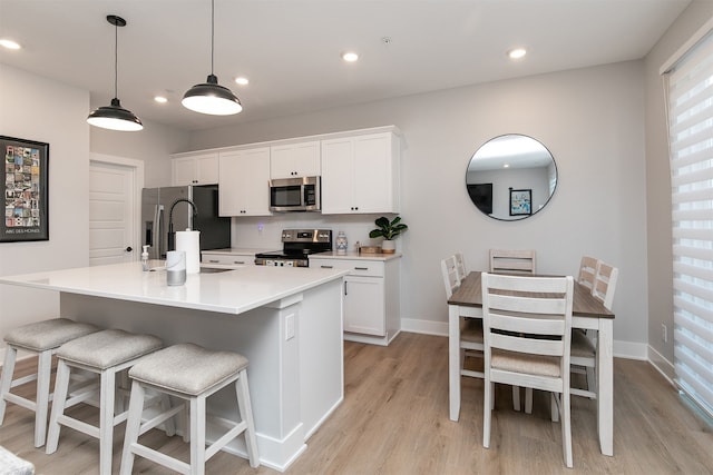 kitchen featuring light hardwood / wood-style floors, appliances with stainless steel finishes, white cabinetry, and a kitchen island with sink