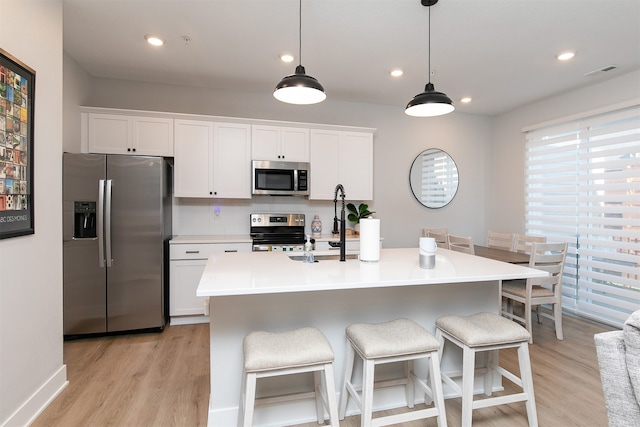 kitchen featuring hanging light fixtures, appliances with stainless steel finishes, white cabinetry, and a kitchen island with sink