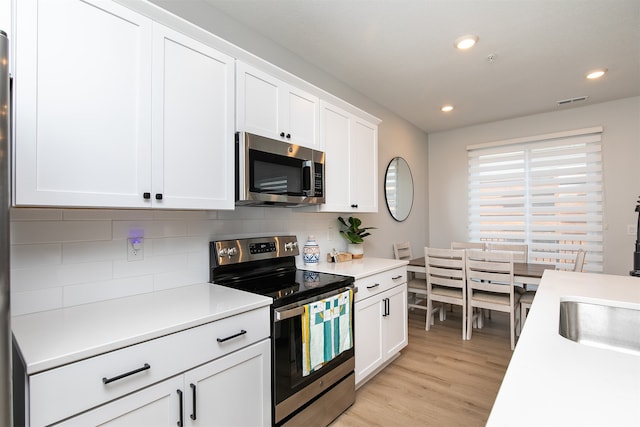 kitchen with light hardwood / wood-style flooring, appliances with stainless steel finishes, white cabinetry, and decorative backsplash