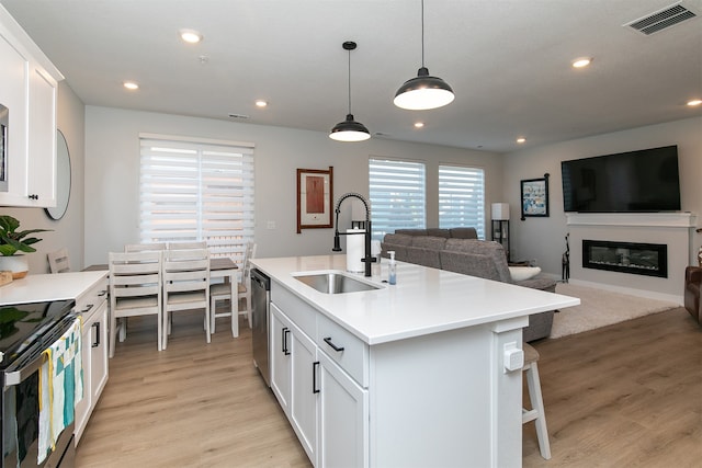 kitchen with decorative light fixtures, light hardwood / wood-style floors, white cabinetry, sink, and an island with sink