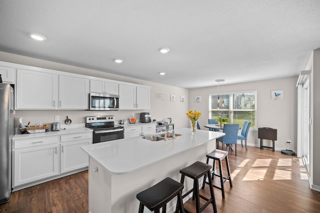 kitchen with a breakfast bar, a sink, dark wood finished floors, appliances with stainless steel finishes, and light countertops