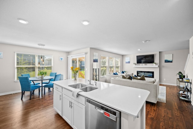 kitchen with dark wood finished floors, a center island with sink, dishwasher, a glass covered fireplace, and a sink