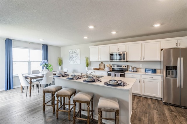 kitchen with a center island with sink, dark wood-type flooring, stainless steel appliances, and white cabinetry