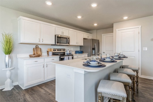 kitchen with dark hardwood / wood-style flooring, stainless steel appliances, white cabinetry, and an island with sink