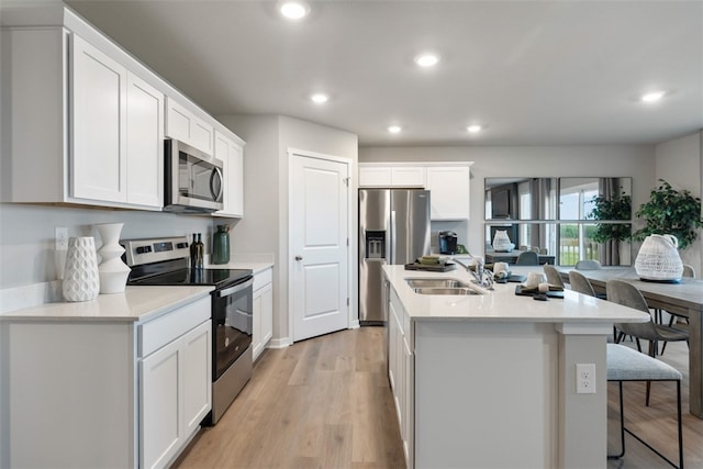 kitchen with a center island with sink, appliances with stainless steel finishes, white cabinetry, light wood-type flooring, and sink