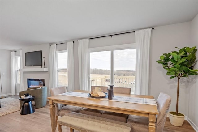 dining space with a glass covered fireplace, light wood-style flooring, and baseboards