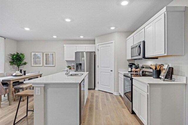 kitchen with a kitchen bar, stainless steel appliances, light hardwood / wood-style floors, white cabinetry, and an island with sink