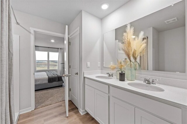 ensuite bathroom featuring double vanity, wood finished floors, a sink, and visible vents