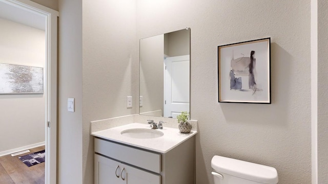 half bath with toilet, wood finished floors, and vanity