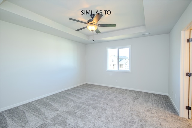 carpeted spare room with a tray ceiling and ceiling fan