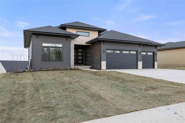 prairie-style house featuring an attached garage, stone siding, concrete driveway, and a front yard