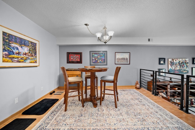 dining area with wood-type flooring, a chandelier, and a textured ceiling