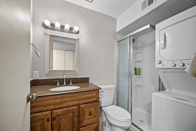 bathroom featuring toilet, a shower with door, vanity, a textured ceiling, and stacked washing maching and dryer