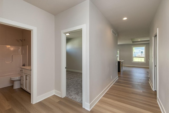 hall featuring light wood finished floors, baseboards, visible vents, and recessed lighting