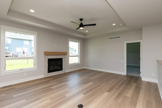 unfurnished living room featuring a tray ceiling, visible vents, and a healthy amount of sunlight