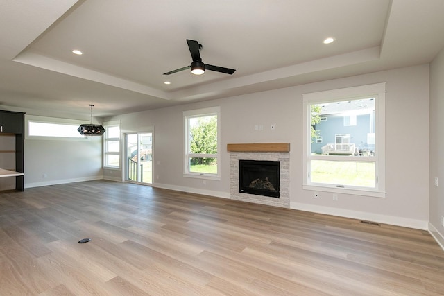 unfurnished living room featuring light wood-style flooring, visible vents, a tray ceiling, and baseboards