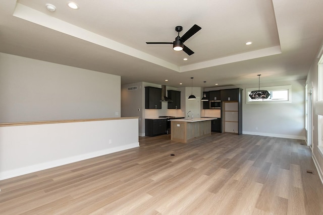 interior space featuring a sink, visible vents, baseboards, a tray ceiling, and light wood finished floors