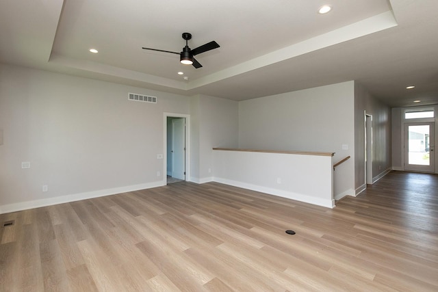 empty room with light wood-style floors, a tray ceiling, visible vents, and baseboards