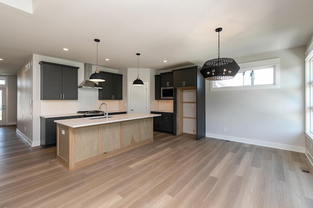 kitchen featuring light wood-type flooring, wall chimney range hood, stainless steel microwave, and light countertops