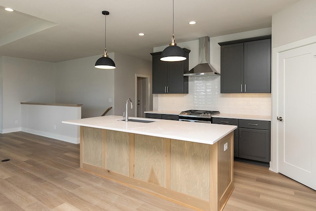 kitchen featuring light wood finished floors, backsplash, a sink, wall chimney range hood, and stainless steel gas range oven