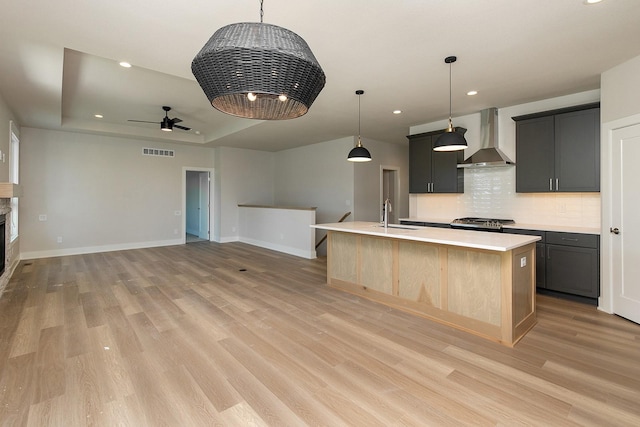 kitchen with a tray ceiling, light countertops, visible vents, a sink, and wall chimney range hood