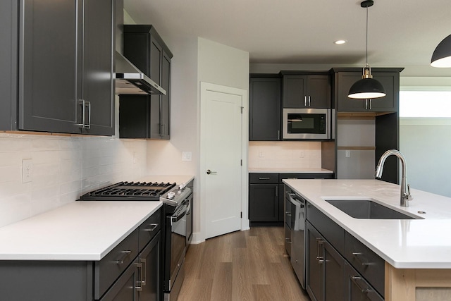 kitchen featuring stainless steel appliances, dark wood-style flooring, a sink, wall chimney range hood, and decorative light fixtures