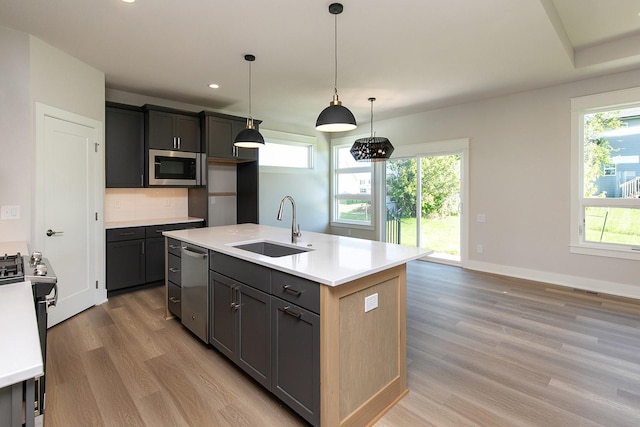 kitchen featuring light wood-style flooring, a sink, light countertops, appliances with stainless steel finishes, and an island with sink