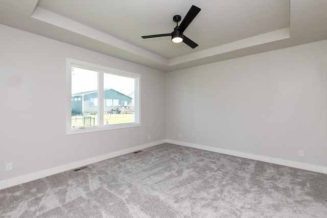 carpeted spare room with ceiling fan, a tray ceiling, visible vents, and baseboards