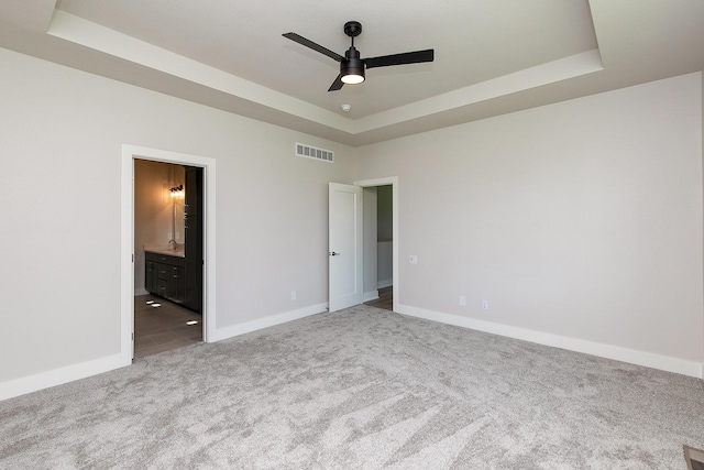 unfurnished bedroom with a tray ceiling, carpet, visible vents, and baseboards