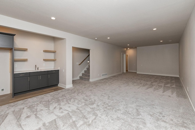 unfurnished living room featuring recessed lighting, a sink, visible vents, baseboards, and stairway