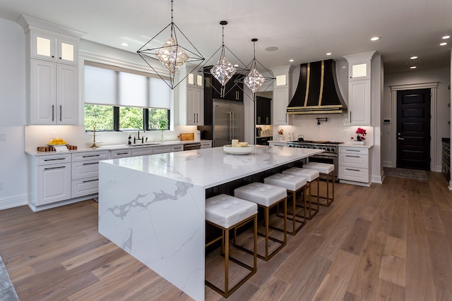 kitchen with high end appliances, custom exhaust hood, a large island, and white cabinets