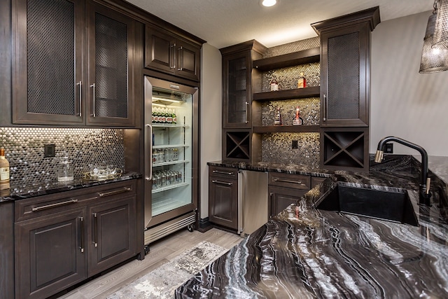 bar with light hardwood / wood-style flooring, sink, decorative backsplash, dark stone countertops, and dark brown cabinetry