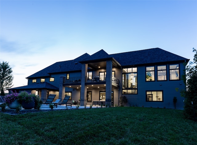 back house at dusk featuring a balcony, a patio area, and a yard